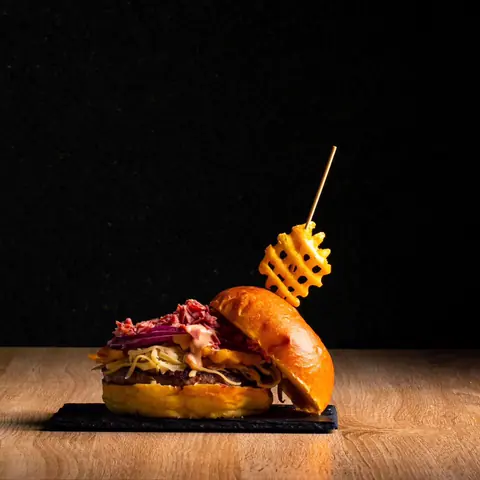 Hamburguesa de Caporale con brioche, pastrami y patata gofre sobre fondo negro